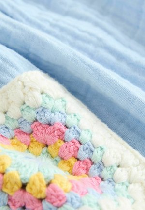 Gehaakte textiel in pastelkleuren—roze, blauw, geel en groen—tegen een lichtblauwe linnen achtergrond, met een gestructureerd patroon.