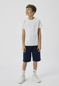 Vit bomulls t-shirt, marinblå shorts och vita sneakers. T-shirten är kortärmad med rund halsringning. Enkelt och grundläggande design.