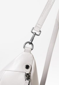 Borsa a tracolla in pelle grigia chiara con forma geometrica, dettagli di cucitura e clip in metallo sulla tracolla. Texture liscia e chiusura con zip.