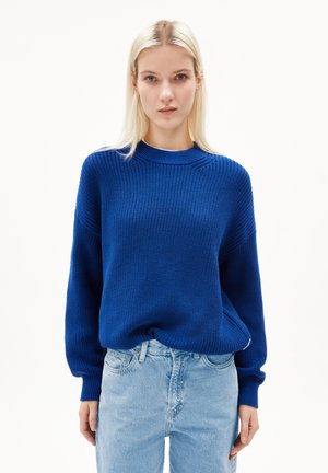 Pull en maille bleue avec un motif texturé, col rond et coupe décontractée. Associé à un jean en denim bleu clair, mettant en avant un style décontracté.