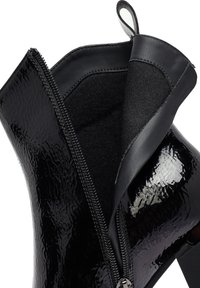 Botín negro con acabado brillante de charol, que presenta una cremallera lateral, un panel elástico y una parte superior texturizada. Tacón de aguja visible en la parte inferior.