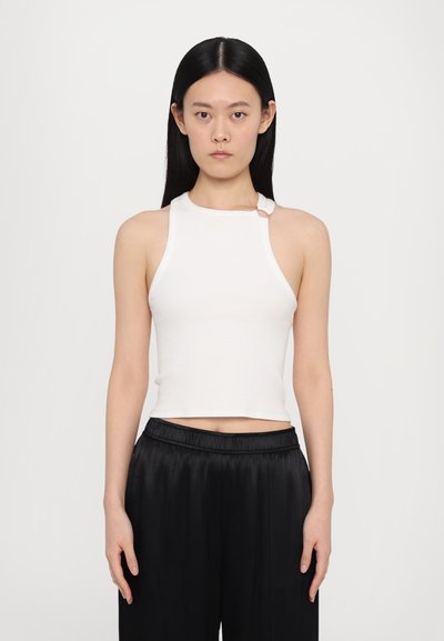 Haut sans manches blanc côtelé avec un col montant et un accent de bouton sur le côté, associé à un pantalon en satin noir. Design simple et ajusté.
