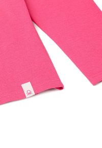 Rosa kurzärmliges Hemd mit glatter Textur, ausgestattet mit einem weißen Etikett am Saum, das ein kleines pinkes Logo zeigt.