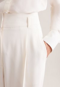 Witte op maat gemaakte broek met een gladde textuur, voorzien van zijzakken en een platte tailleband. De stof lijkt lichtgewicht en slank.