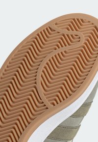 Schuhsohle mit einem wellenförmigen Gummimuster in Hellbraun, mit weißen Randdetails und strukturierten grauen Abschnitten im oberen Bereich.