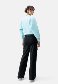 Lichtblauw cropped sweatshirt met elastische zoom, gecombineerd met zwarte wijde broek met cargozakken en witte sneakers.