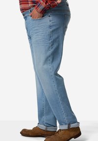 Vaqueros de mezclilla de un azul claro con un corte relajado, con un ligero desgaste, cinco bolsillos y puños enrollados, combinados con zapatos marrones de cordones.