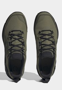 Sportovní boty olivově zelené barvy s texturovaným látkovým svrškem, černými tkaničkami a kontrastními černými podrážkami. Hladká, zaoblená špička a polstrovaná stélka.