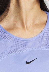 Nära bild av en persons nacke och övre bröst med en lavendelfärgad Nike sporttop med meshdetaljer och en svart Nike swoosh-logotyp.