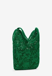 Vihreä virkattu laukku, jossa on kukkakuvioita, pehmeää kangasta ja kaksi pyöreää kahvaa. Kevyt ja avoin muotoilu helppoon pääsyyn.