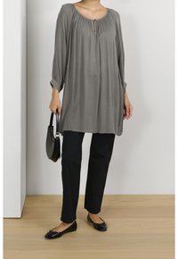 Túnica gris de ajuste holgado, con escote tipo ojal y diseño plisado, combinada con pantalones rectos negros y bailarinas negras.