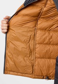 Isolering av jackans inre i varm brun färg, med kviltad textur och en sidoficka med dragkedja för säker förvaring.