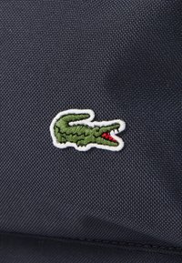 Marineblauwe gestructureerde stof met een groene krokodillenlogo omlijnd in wit, met een rode accentdetail.