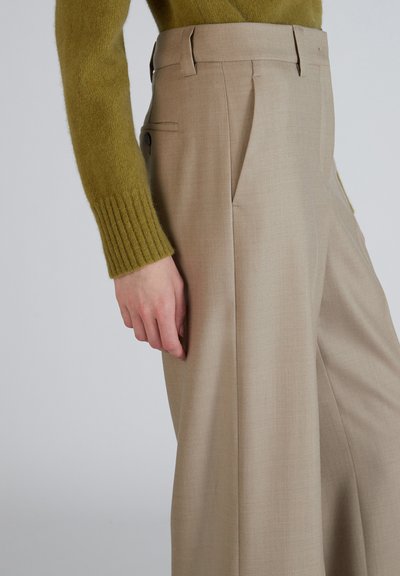 Beige op maat gemaakte broek met een vlakke voorkant, plooien en zijzakken, gecombineerd met een groen, gestructureerd breiwerk trui.