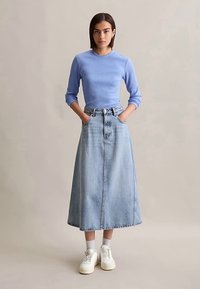 Ljusblå ribbad långärmad topp kombinerad med en helfots jeanskjol. Outfiten har hög midja och sidofickor, och bärs med vita sneakers.