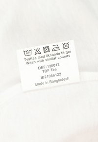 Vit tvättetikett med skötselråd och detaljer, inklusive temperaturinstruerande, textilvårdsymboler och tillverkningsland.