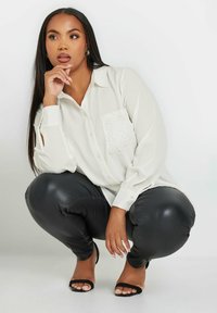 Camicia bianca a maniche lunghe con dettaglio in tessuto nel taschino, abbinata a leggings neri lucidi e sandali neri a ciabatta. Tessuto morbido e vestibilità comoda.