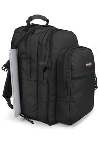 Mochila negra hecha de tela resistente, con múltiples compartimentos, con forma de fondo plano, bolsillo lateral y asa en la parte superior.