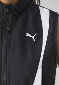 Crna bezrukavna jakna s visokim ovratnikom, sa prednjim zatvaračem i kontrastnim bijelim bočnim prugama. Puma logo se ističe.