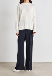 Krämfärgad stickad tröja med sänkta axlar, kombinerad med marina vida byxor. Tröjan har ribbade ärmslut och nederkant, samt en mjuk textur.