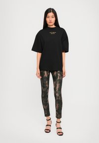 T-shirt oversize nera con logo in testo dorato, abbinata a leggins attillati con texture e motivo scuro e sandali neri con punta aperta.