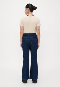 Beige T-särk maroon kaelusega, paari tumedate siniste flare-tehnika teksadega, millel on tagakotid ja sile tekstuur. Mustad platvormkingad.