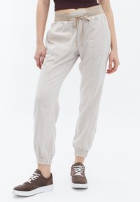 Lichtgrijze joggerbroeken met een elastische tailleband en trekkoord, voorzien van zijzakken en elastische boorden bij de enkels. Gestyled met bruine sneakers.