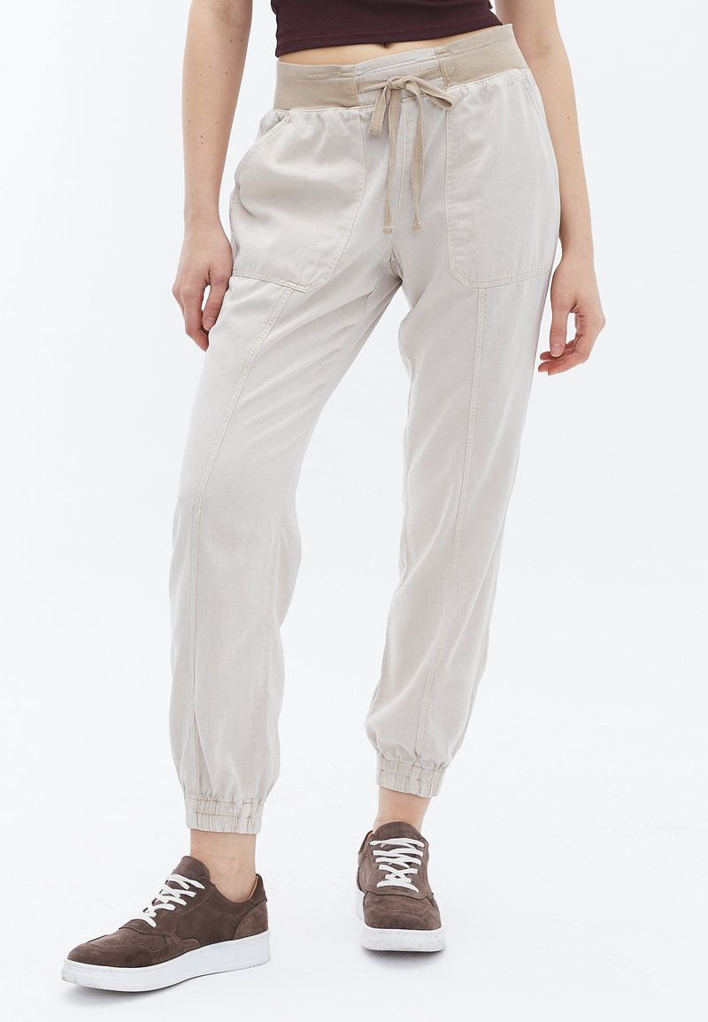 Lichtgrijze joggerbroeken met een elastische tailleband en trekkoord, voorzien van zijzakken en elastische boorden bij de enkels. Gestyled met bruine sneakers.