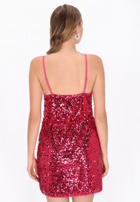 Élénk rózsaszín flitteres ruha, vékony pántokkal és testhez simuló fazonnal, fényes, texturált felülettel és ráncolt derékvonallal.