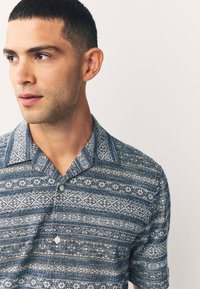 Kurzärmeliges Hemd zum Knöpfen in Blau mit komplexen weißen und braunen geometrischen Mustern, ausgestattet mit einem Kentkragen und strukturiertem Stoff.