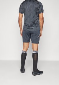 Outfit sportivo composto da una maglietta a maniche corte grigia scura con motivo, pantaloni corti abbinati con righe laterali e calzini neri con righe bianche. Scarpini in vista.