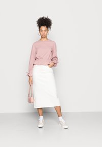 Pink long-sleeve top with elastic waist and ruffled cuffs, paired with a white midi skirt and light sneakers. Small pink handbag included.
