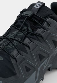 Schwarzer Sportschuh mit strukturiertem Obermaterial, ausgestattet mit einem schnellen Schnürsystem, verstärktem Zehenbereich und geometrischem Muster auf der Sohle.