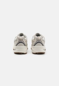 Sneaker mit einem beigefarbenen Mesh-Obermaterial, grauen Akzenten und gemustertem Fersenbereich. Verfügt über eine dicke weiße Sohle mit strukturiertem Grip und gepolstertem Kragen.