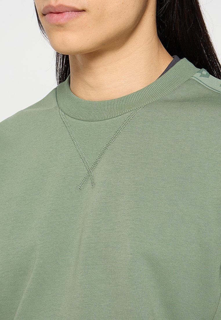 Zielona bawełniana bluza z okrągłym dekoltem, z wyraźnymi detalami szycia i luźnym krojem. Minimalistyczny design bez wzorów.