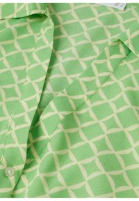Blouse à motif vert avec un design géométrique et des accents jaune pâle. Fabriquée en tissu léger avec un col et des détails à boutons.