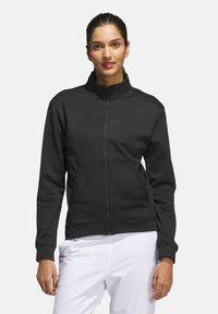 Black zip-up jacket with high collar, made of smooth fabric. Features two front pockets and ribbed cuffs. Simple, functional design.