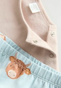 Helles rosa Oberteil mit Druckknopfverschluss und kurzen Ärmeln über einem blauen Unterteil mit einem bedruckten braunen Kuhdesign. Weiches, aus Baumwolle gemischtes Material.