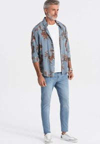 Kortärmad, ljusblå blommig skjorta över en vit T-shirt, kombinerad med ljusblå jeans och grå/vita sneakers. Avslappnad design, loose fit.