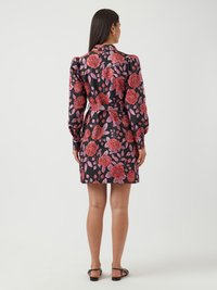Robe noire à fleurs avec des manches longues, ornée de grandes roses roses et de feuillages verts, taille cintrée et longueur courte. Texture du tissu lisse.