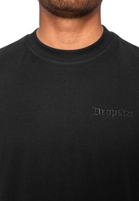 Sort bomuld T-shirt med rund hals, korte ærmer og et præget "Dropsize" logo på venstre bryst. Glat tekstur.