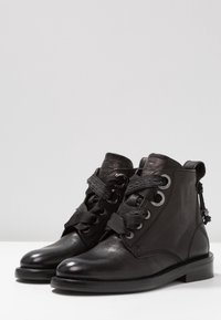 Las botas de tobillo de cuero negro presentan una puntera redondeada, un sistema de cierre con ojales y cintas decorativas, y un tacón bajo apilado.