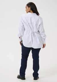 Camisa de rayas de manga larga en blanco y azul marino con un diseño de espalda recogida, combinada con jeans de mezclilla oscura y zapatos negros.