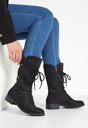 Bottines en suède noir avec un bout rond, un laçage à l'avant, une fermeture éclair sur le côté et une semelle plate. Comprend des détails de couture et des accents en ton argent.