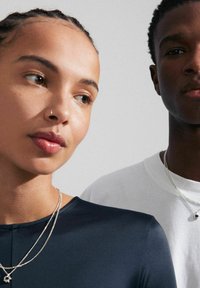 Marinblå åtsittande topp med rund halsringning, kompletterad med lager av silverhalsband. En vit t-shirt med minimalistisk design bärs av personen till höger.
