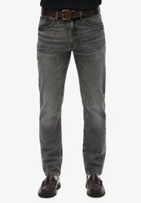 Jeans de denim gris con corte recto, detalles sutiles de desgaste, diseño de cinco bolsillos y un cinturón de cuero marrón. Combinados con mocasines oscuros.