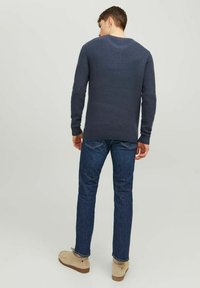 Marineblå strikket sweater med struktureret design, ribbede manchetter og kant. Kombineret med mørkeblå jeans og beige casual fodtøj.