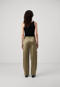 Cargo pants in licht olijfgroen, met een hoge taille, wijde pijpen, twee zijzakken en een zachte, gemêleerde stof. Een zwarte tanktop wordt gedragen.