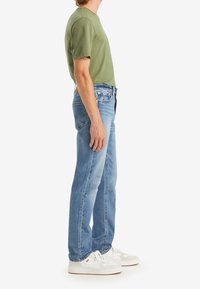 Grön bomulls-t-shirt, blå jeans i denim och vita sneakers. Jeansen har klassisk passform och subtil sömnad, t-shirten har korta ärmar.