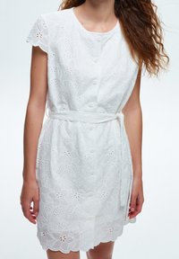 Vitt bomullsklänning med blommigt broderi, korta cap sleeves, knäppning framtill och ett tygbälte vid midjan med scallopad nederkant.